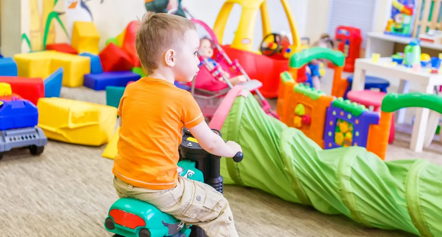 boy child sitting on top of a toy motorcycle looking at his play room full of toys