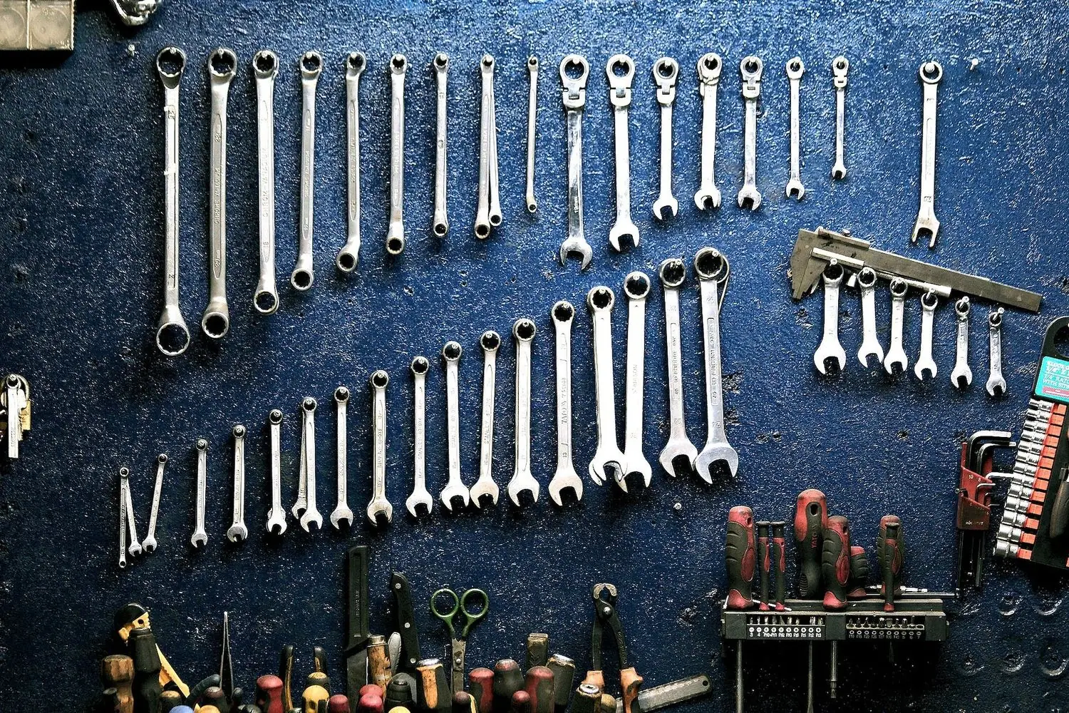 Spanners hung in size order across a blue pegboard wall, with screwdrivers, pliers and a socket set below