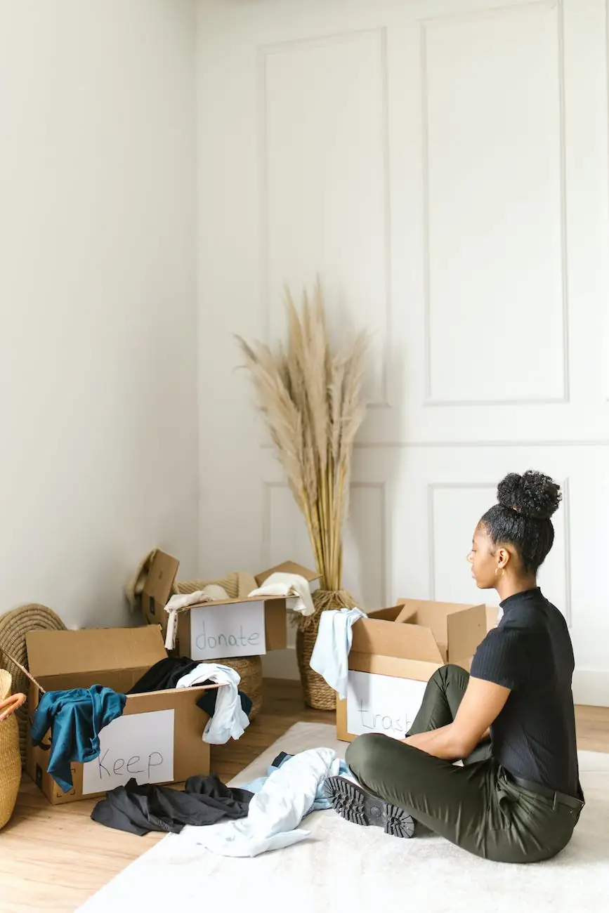 A woman sitting on the floor beside cardboard boxes hand-labelled keep, donate and trash, sorting a pile of clothes
