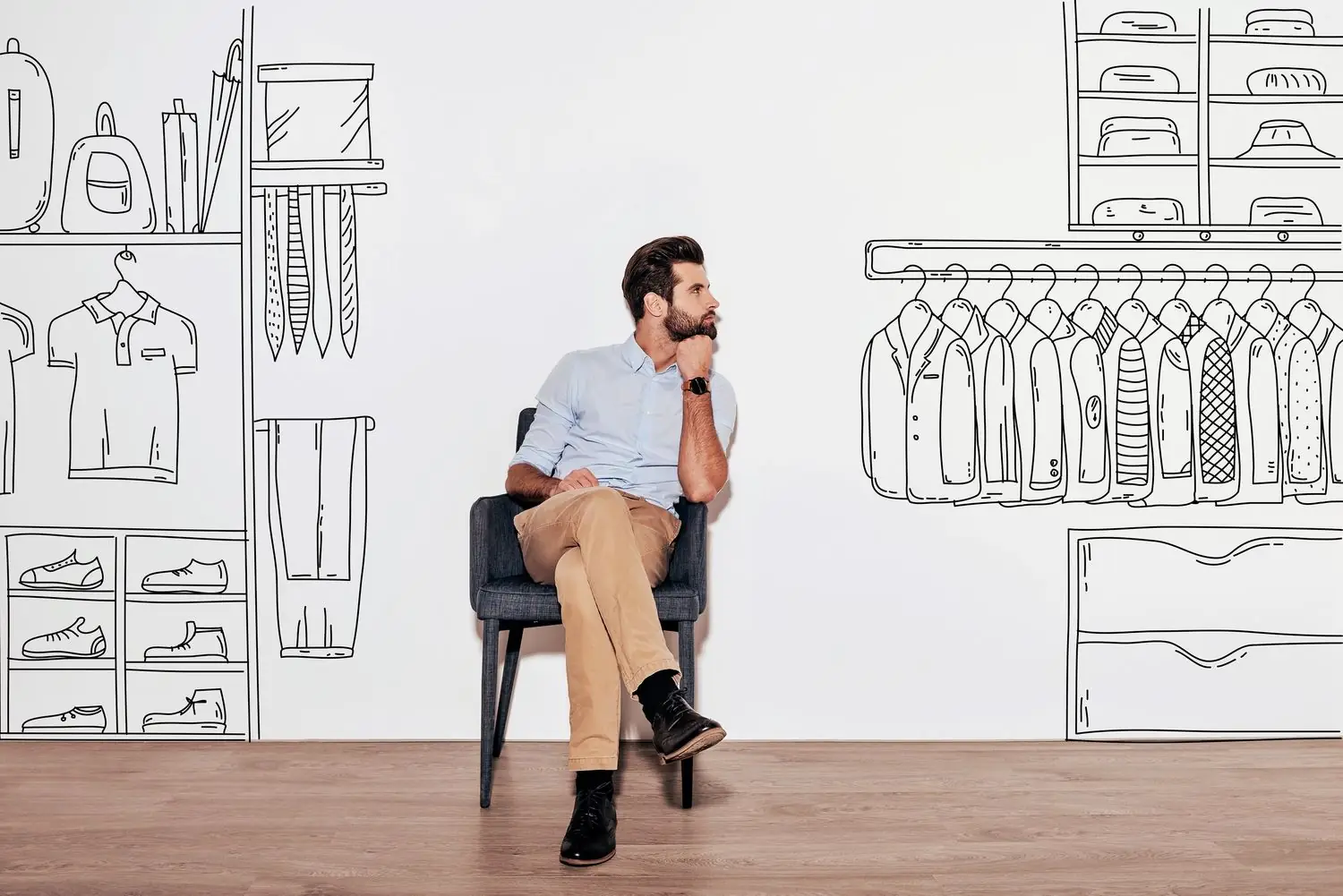 Young handsome man keeping hand on chin and looking away while sitting in the chair against illustration of an organized closet in the background